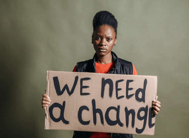 Black woman holding 'we need a change' sign